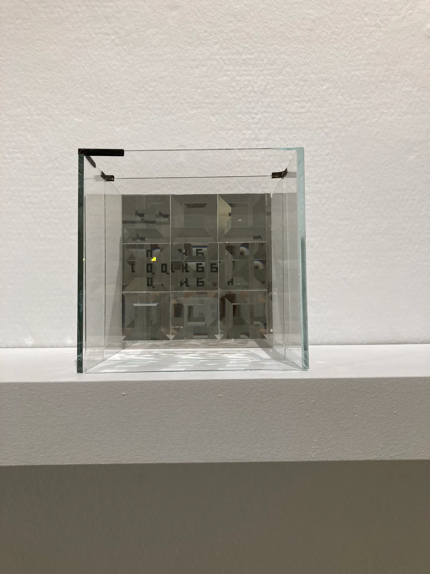 Top-down view into a transparent glass cube containing an array of faceted glass prisms with Cyrillic letterforms