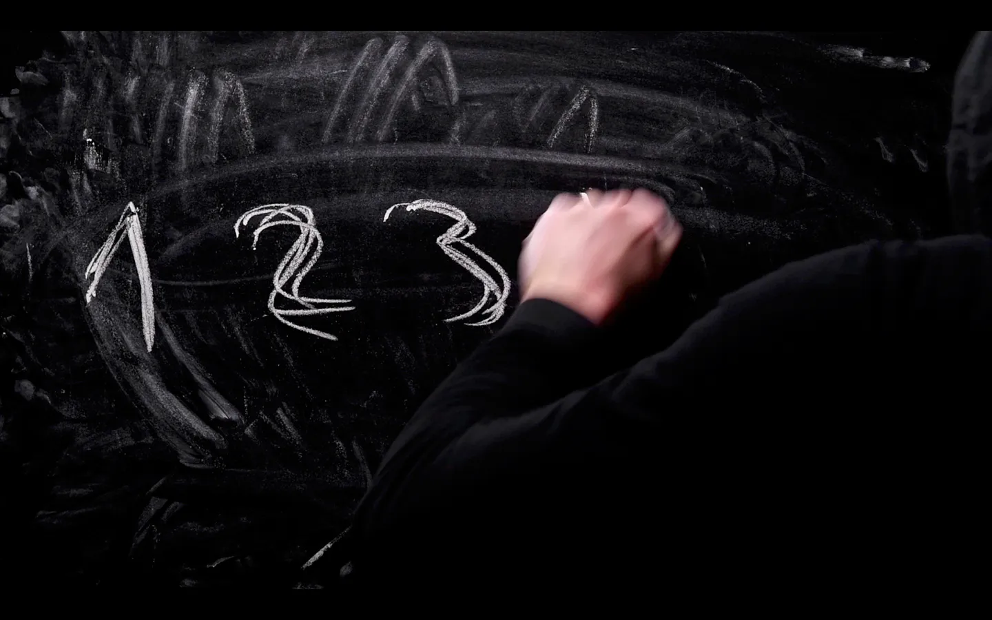Close-up of a person writing the numerals 1, 2, and 3 in white chalk on a smudged blackboard
