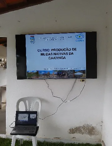 Laptop connected to a wall-mounted television screen showing the seedling production lecture slide.
