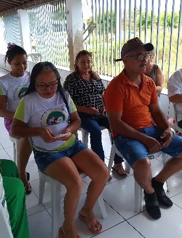 Community members seated in plastic chairs attentively following the classroom presentation.