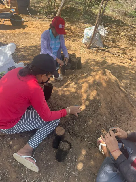 Women seated on the ground filling black nursery bags with prepared soil substrate.