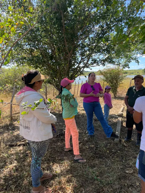 Instructor speaking with community members gathered under a tree beside the water reservoir.